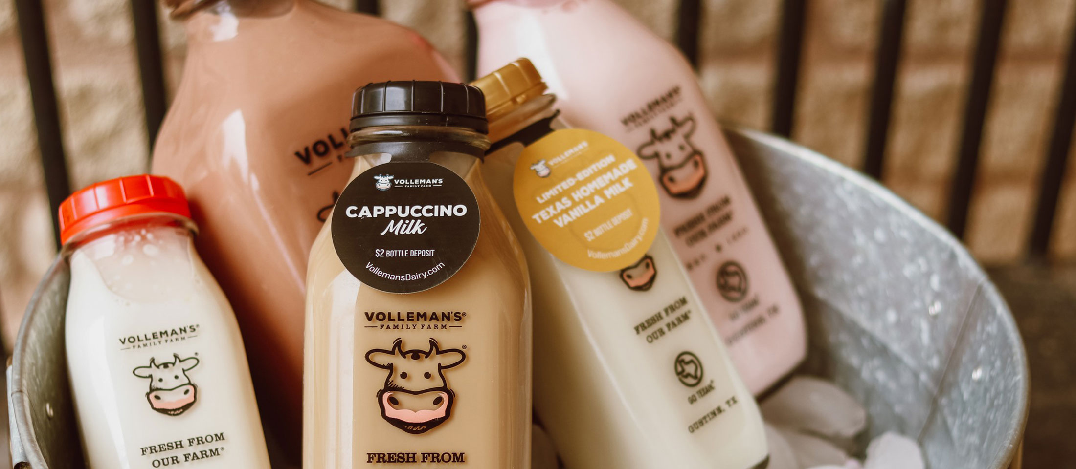 5 botellas de vidrio que muestran diferentes sabores de leche en un balde que se enfría en hielo.
